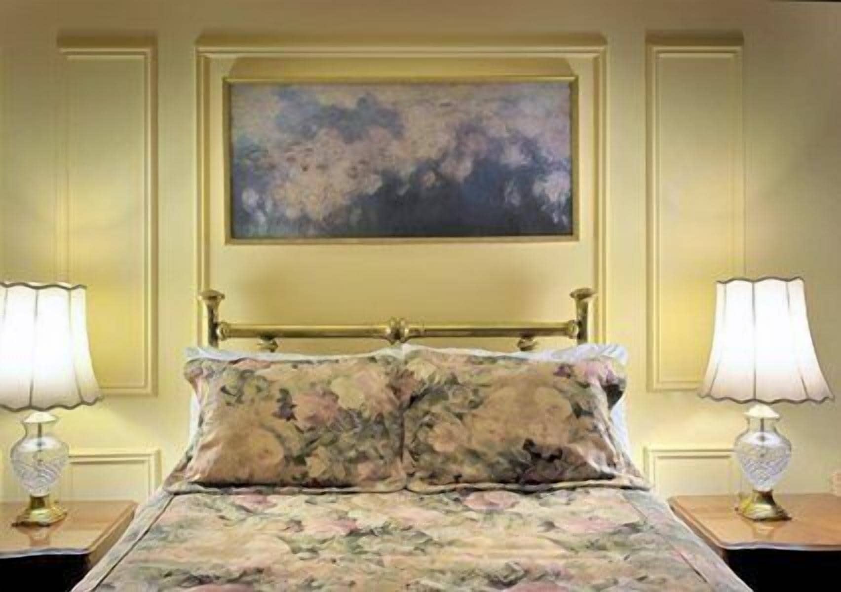 A bed with floral bedding, a painting above it, and two bedside lamps on either side.