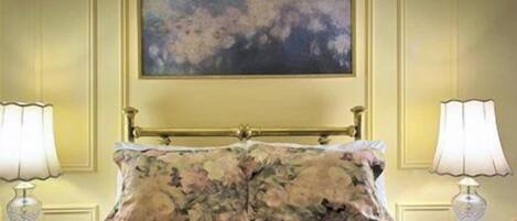 A bed with floral bedding, a painting above it, and two bedside lamps on either side.