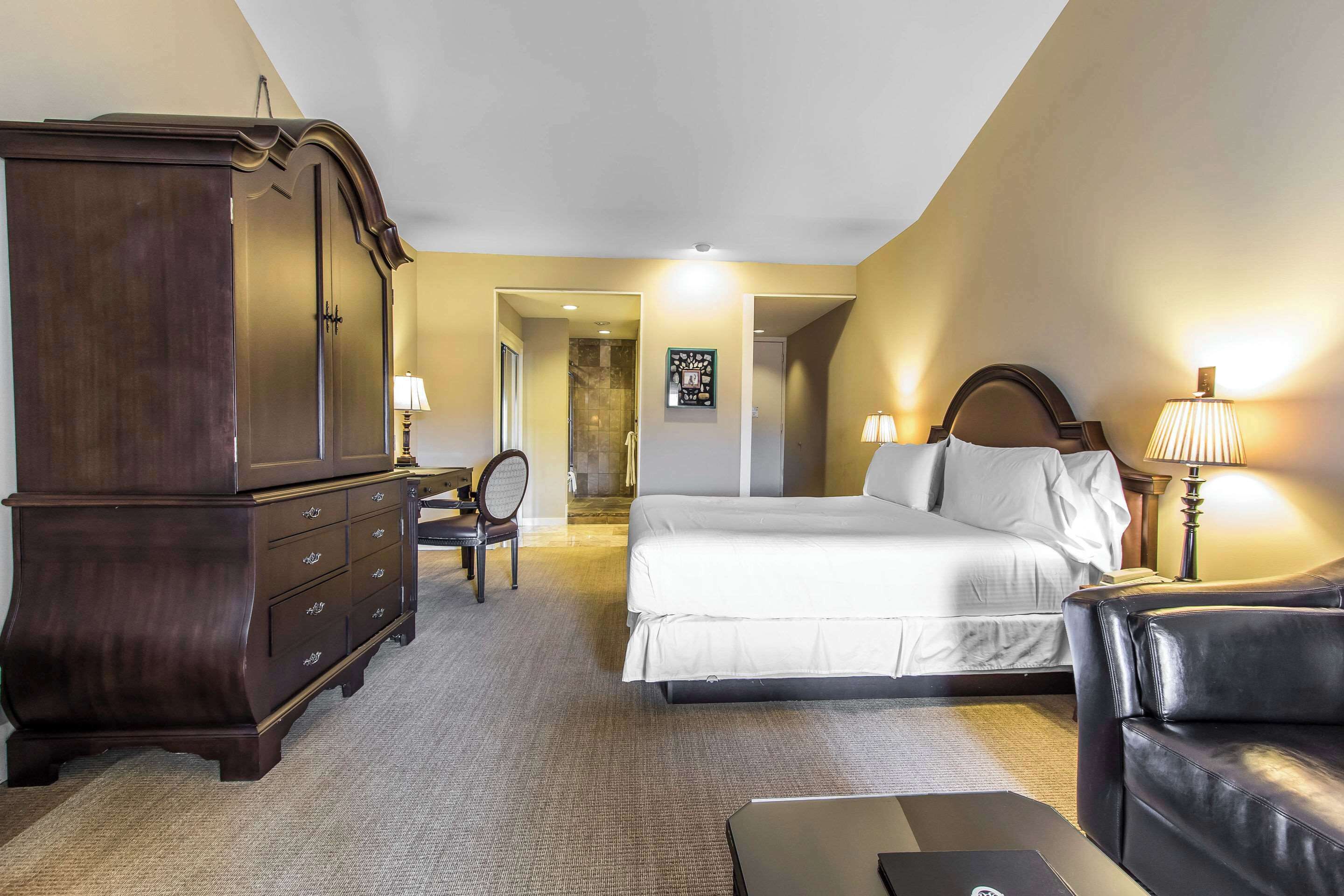 A hotel room with a large bed, a dark wooden dresser, a leather sofa, and a desk with a lamp.