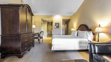 A hotel room with a large bed, a dark wooden dresser, a leather sofa, and a desk with a lamp.