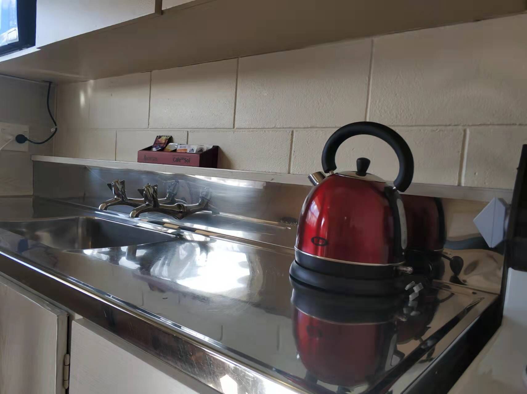 A stainless steel kitchen sink with a red kettle and a coffee machine.
