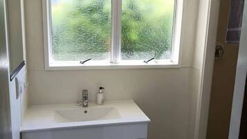 A bathroom with a white vanity, a window with frosted glass, and a shower area.