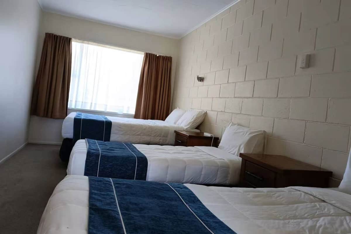 Habitación de hotel con dos camas, una ventana con cortinas, un pared con diseño de ladrillo y una mesita de noche pequeña.