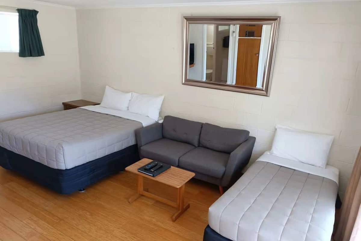 Una habitación con dos camas, un sofá, una mesita, un espejo y una ventana con cortinas.