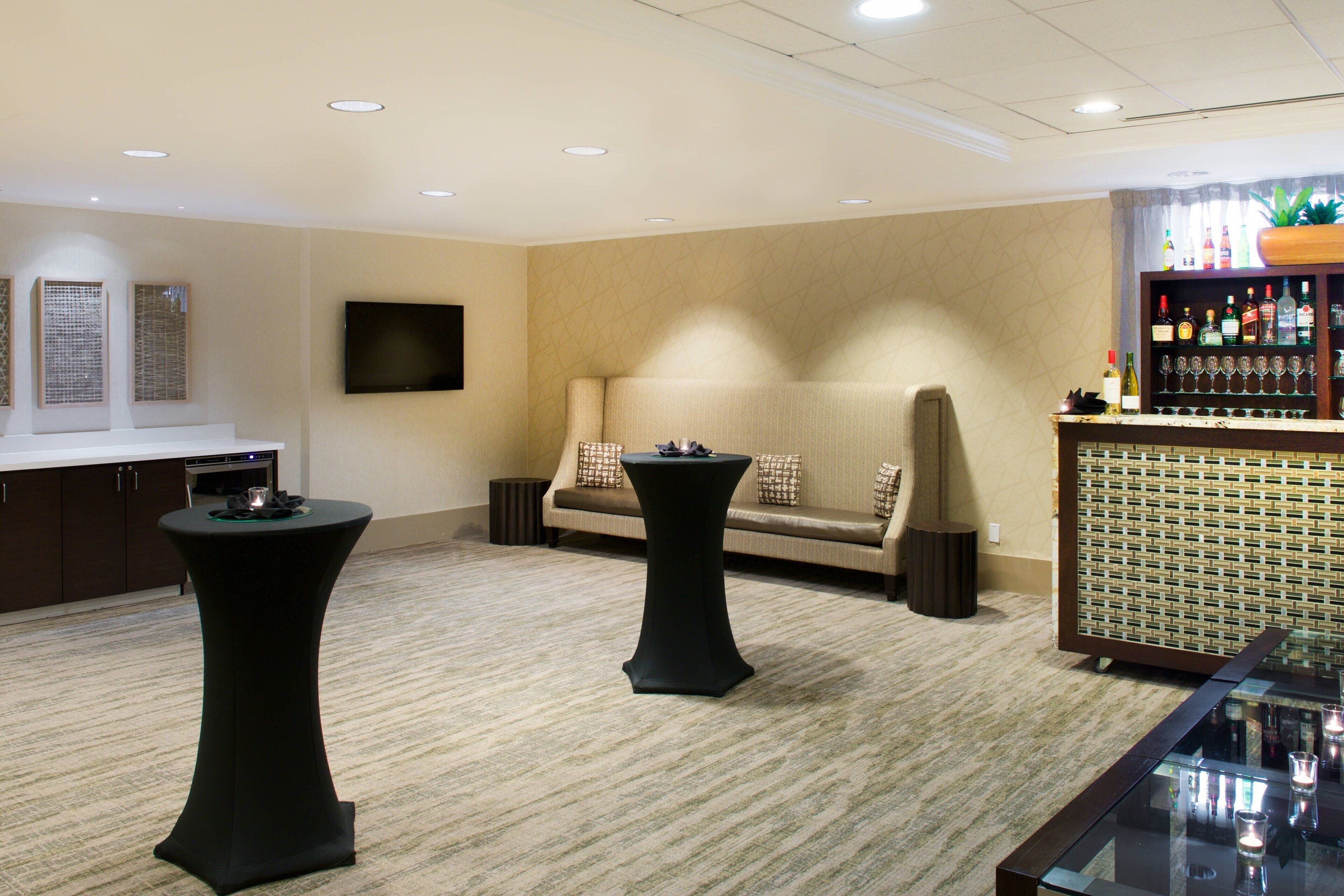 A room with a sofa, two round tables, a TV, and a bar area with bottles and glasses.