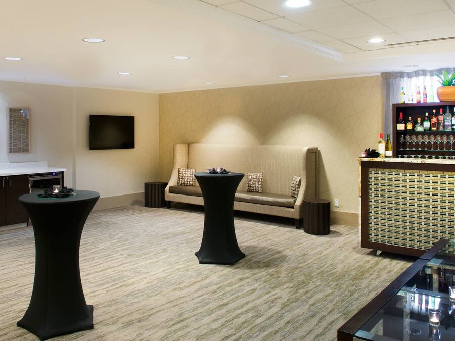 A room with a sofa, two round tables, a TV, and a bar area with bottles and glasses.