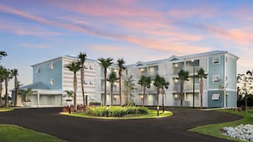 A multi-story hotel with a curved driveway, palm trees, and a well-maintained lawn.
