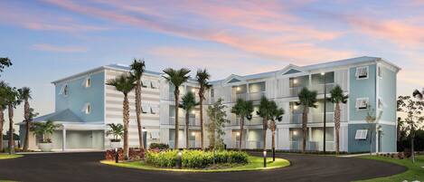 A multi-story hotel with a curved driveway, palm trees, and a well-maintained lawn.