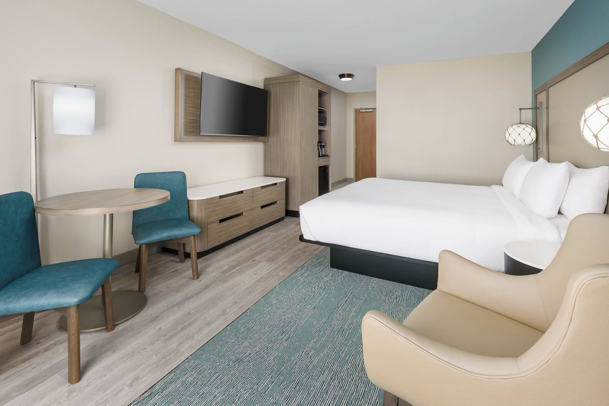 Una habitación de hotel con cama, escritorio con sillas, televisor y armario.