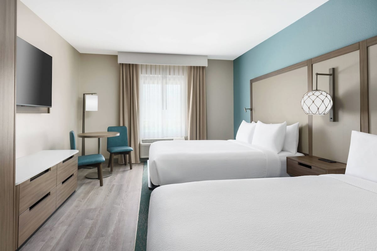 Habitación de hotel con dos camas, un escritorio, una silla, un televisor y una ventana con cortinas.