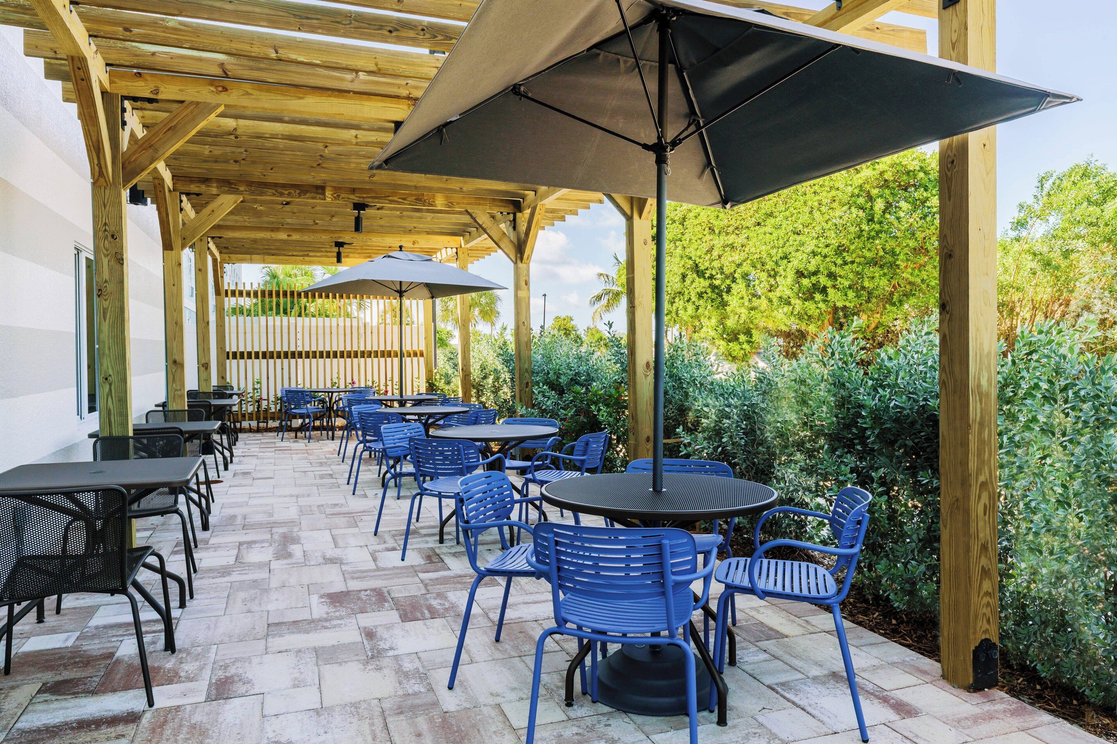 An outdoor patio with wooden pergola, tables, and blue chairs.