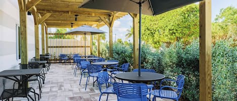 Une terrasse extérieure dotée d’une pergola en bois, de tables et de chaises bleues.