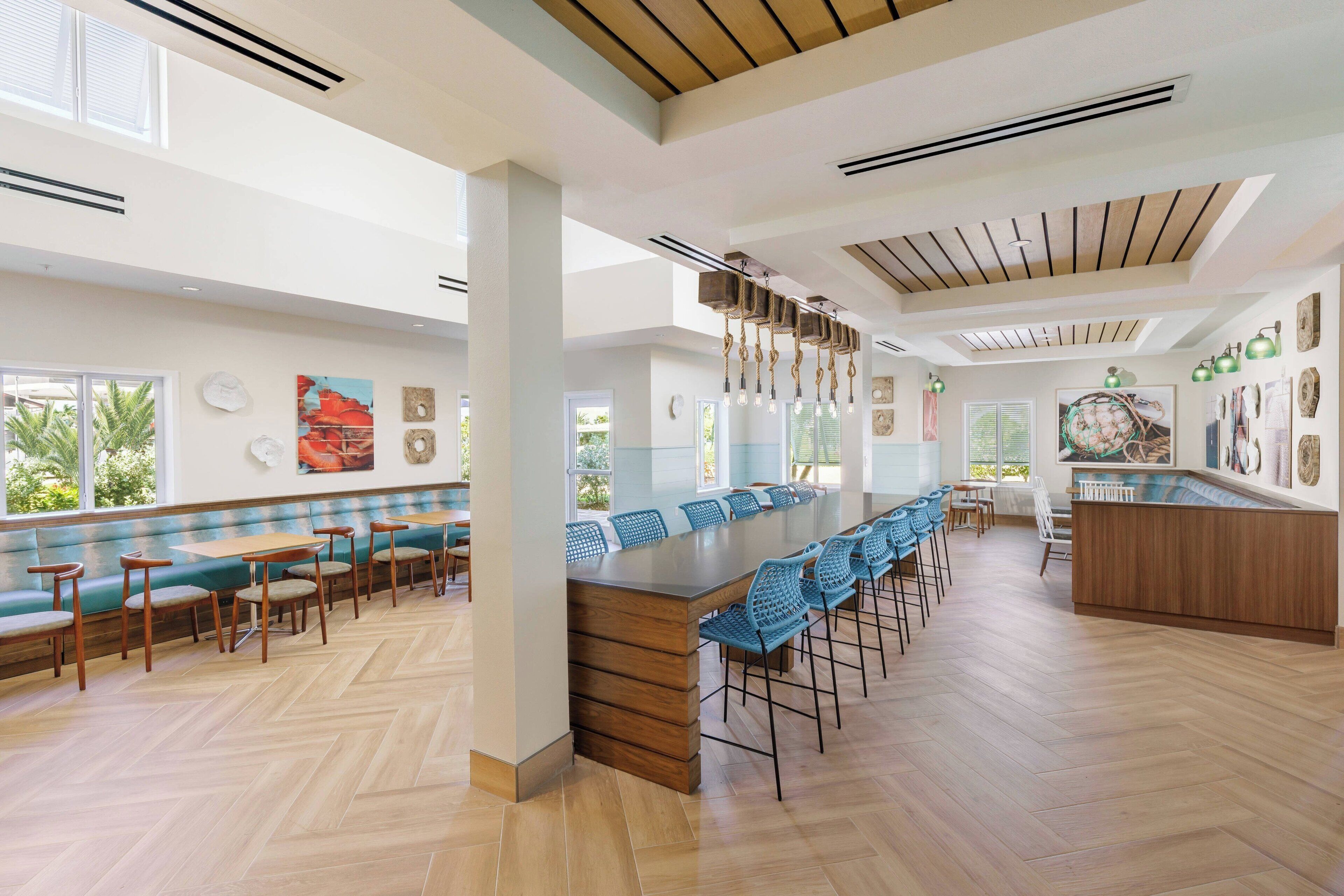 A spacious indoor area with a long wooden bar, blue chairs, and a seating area with green sofas and wooden tables.