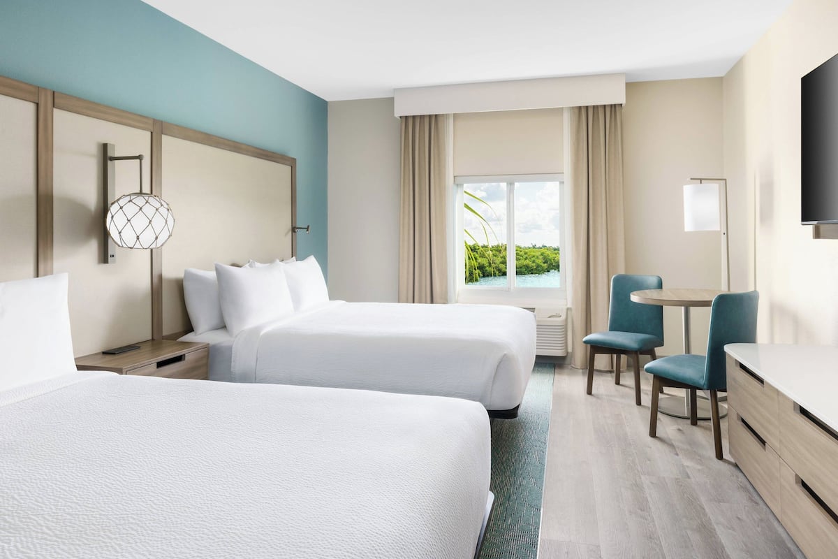 Habitación de hotel con dos camas, un escritorio, una silla y un televisor.