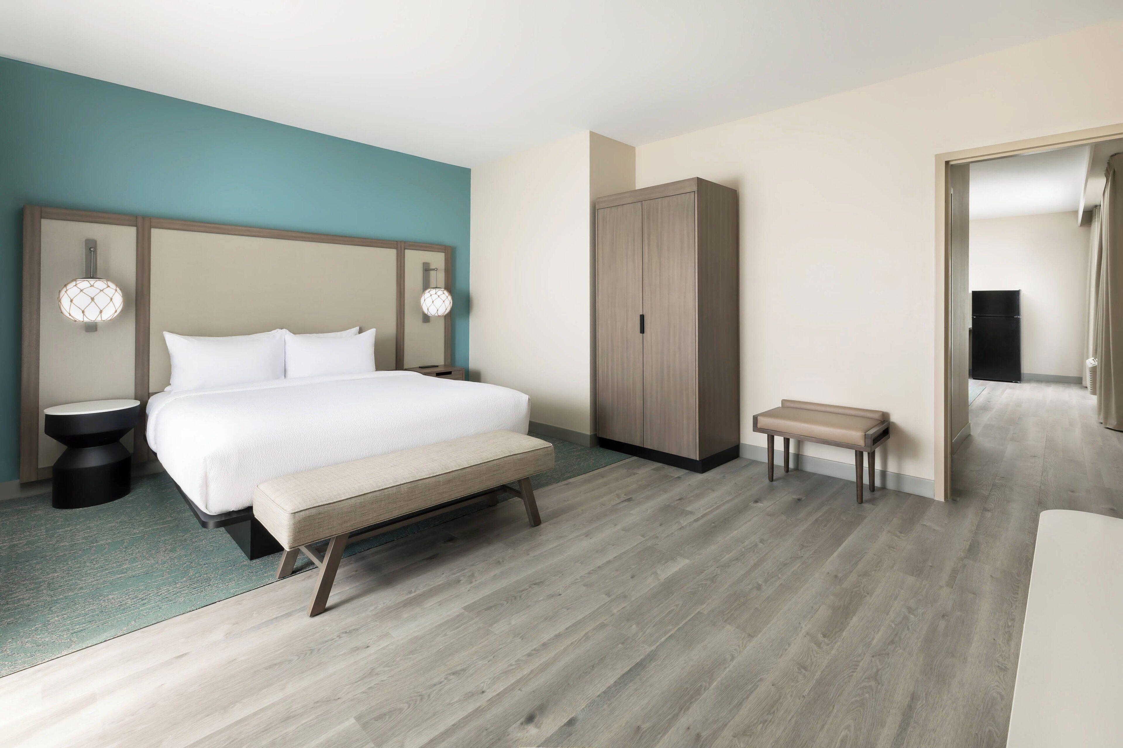 A modern hotel room with a large bed, bedside tables, a bench, a wardrobe, and a mirror.