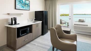 A modern kitchen with a microwave, refrigerator, and coffee maker. There is a chair and a balcony with a view of the water.