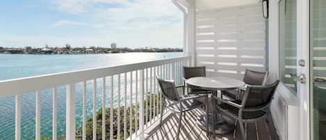 A balcony with a view of the ocean, a round table, and two chairs.