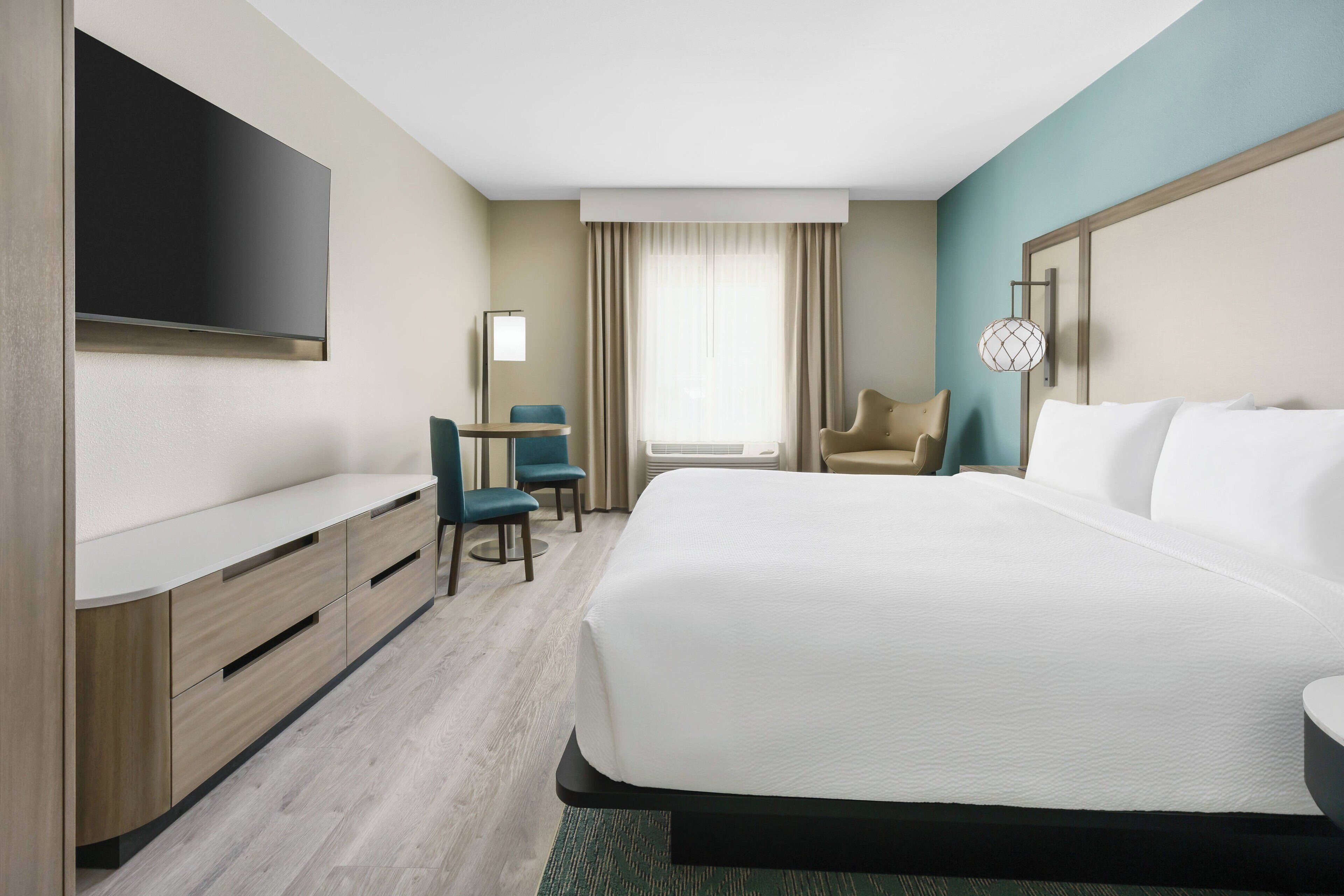 Habitación de hotel con una cama grande, un televisor de pantalla plana en la pared, un escritorio con una silla y una ventana con cortinas.