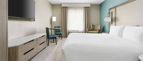 Habitación de hotel con una cama grande, un televisor de pantalla plana en la pared, un escritorio con una silla y una ventana con cortinas.