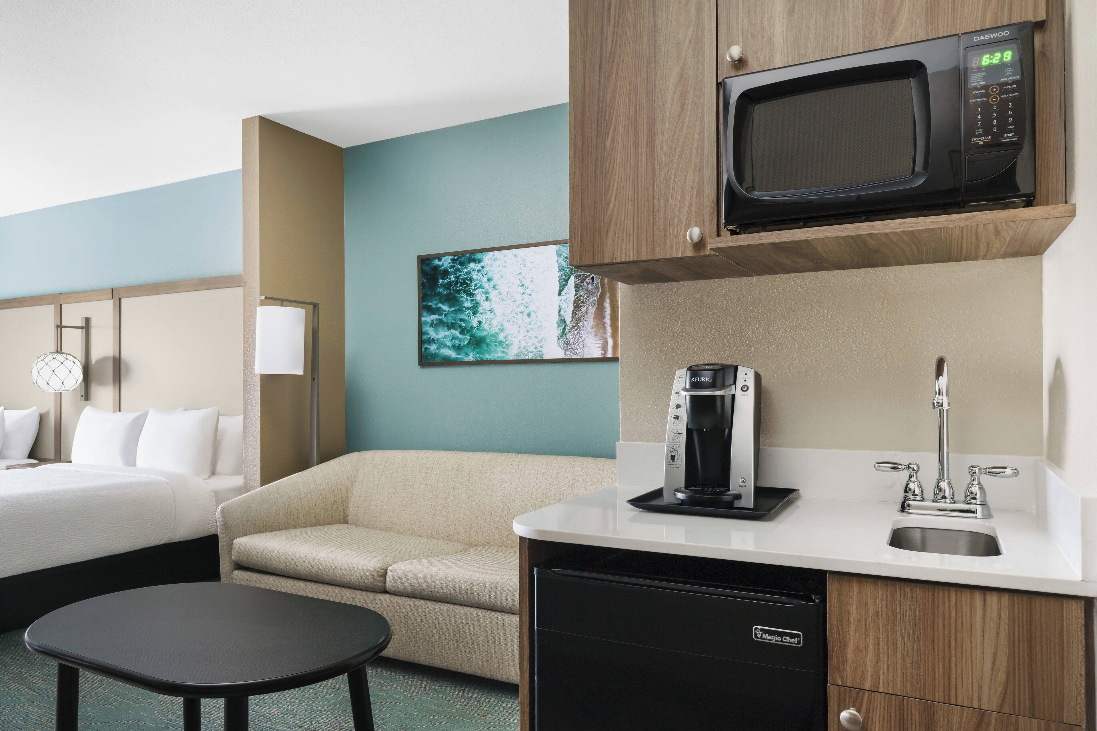 Quarto de hotel com uma cama, um sofá, uma mesinha, micro-ondas, cafeteira e máquina de lavar louça.