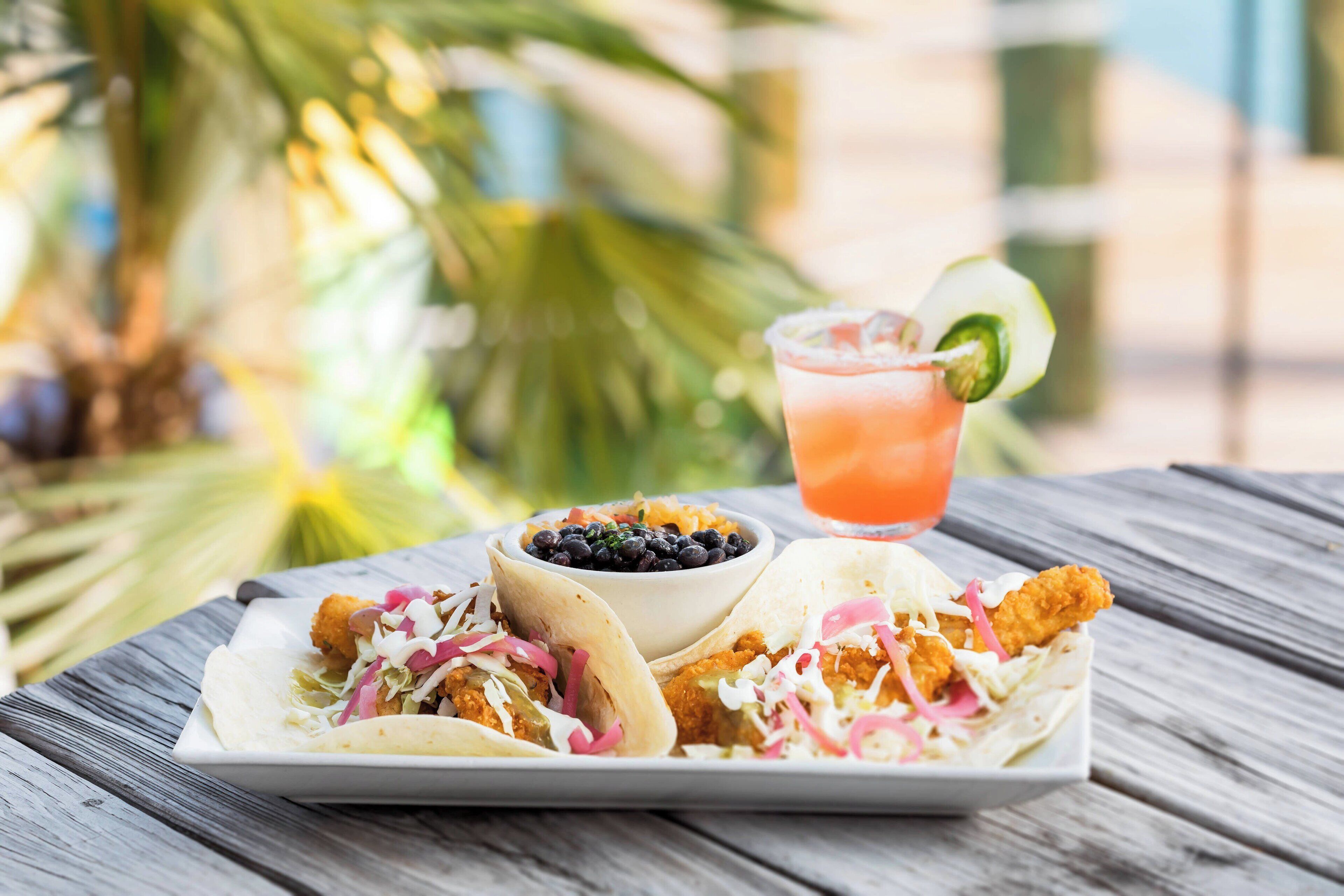 Une assiette de tacos, accompagnée d’une portion de haricots noirs et d’une boisson avec une tranche de citron vert.