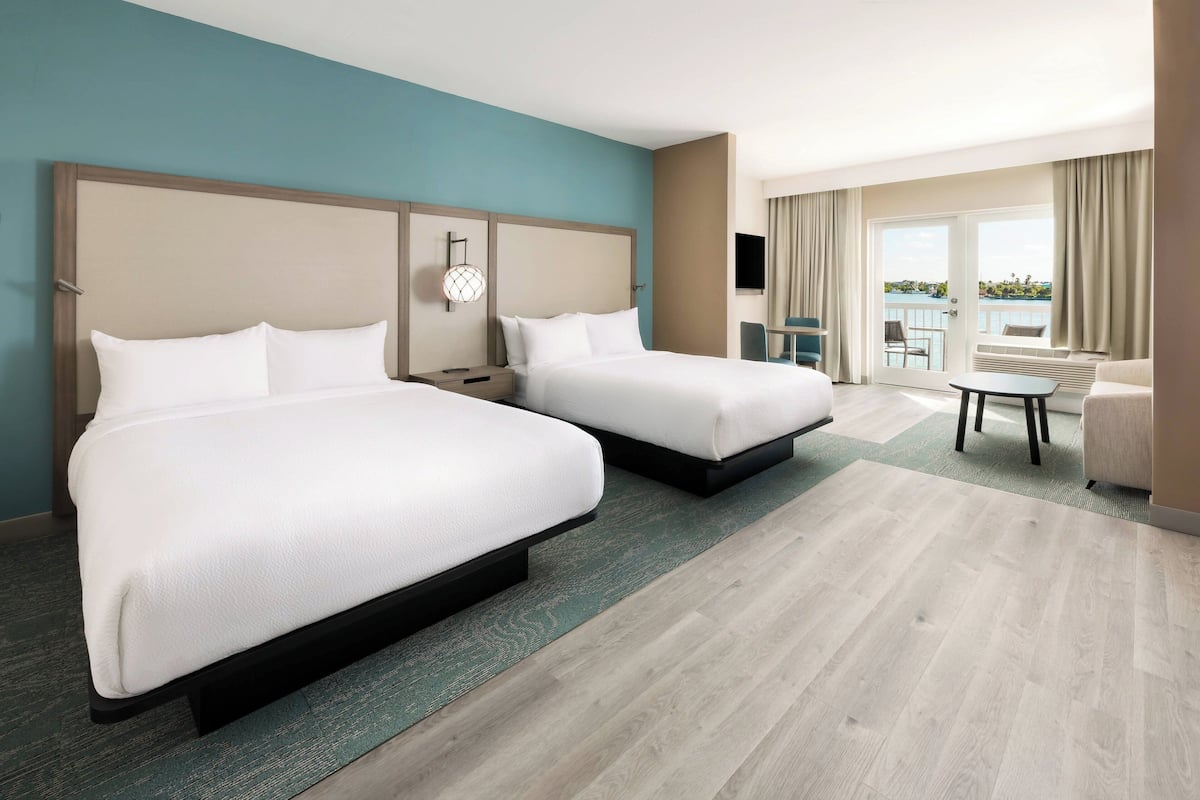 Habitación de hotel con dos camas, una mesita, una silla y balcón con vistas.