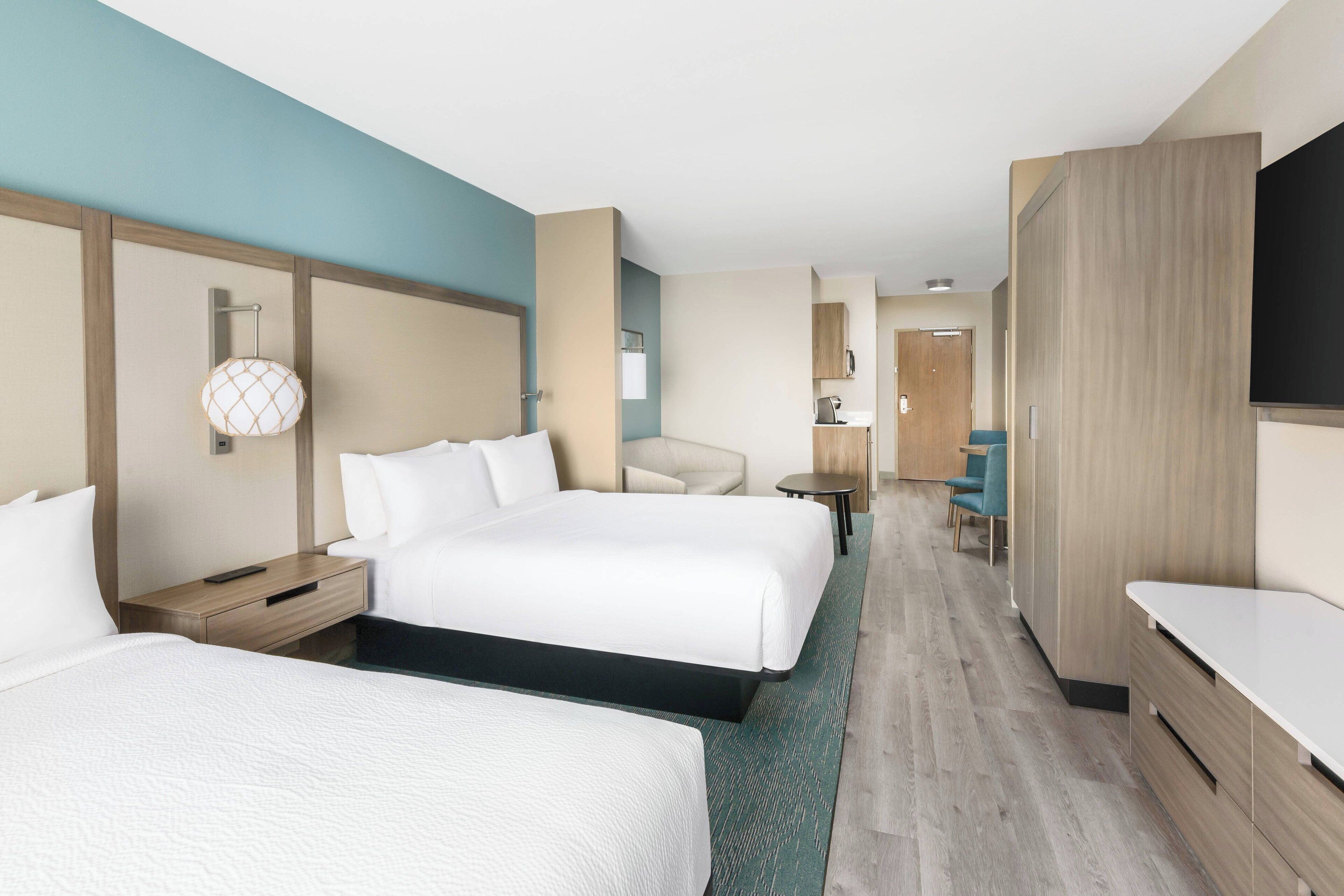 Una habitación de hotel con dos camas, un escritorio, una silla, un televisor y un minibar.