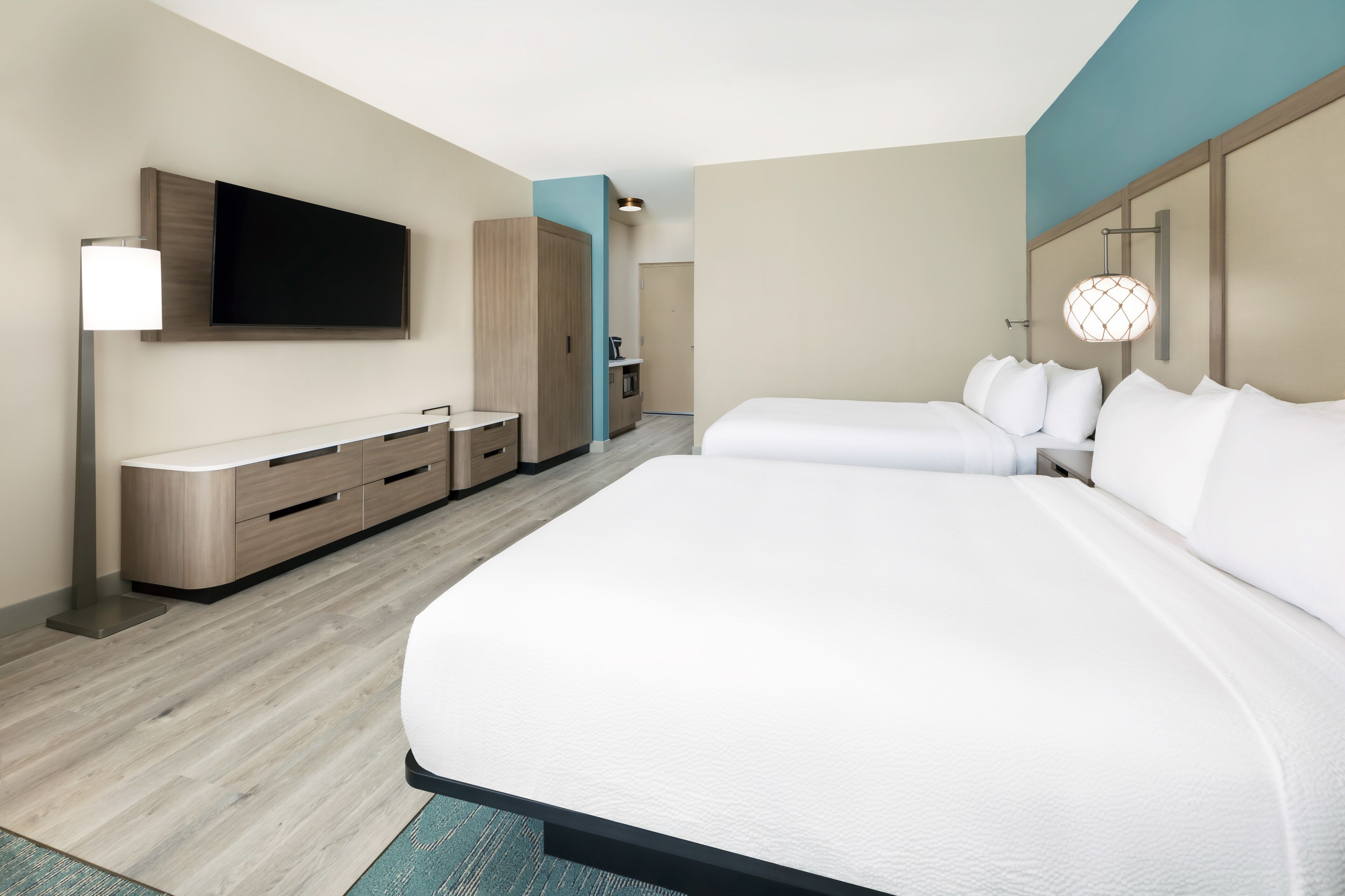 A modern hotel room with a large bed, a flat-screen TV mounted on the wall, a bedside table, and a wardrobe.