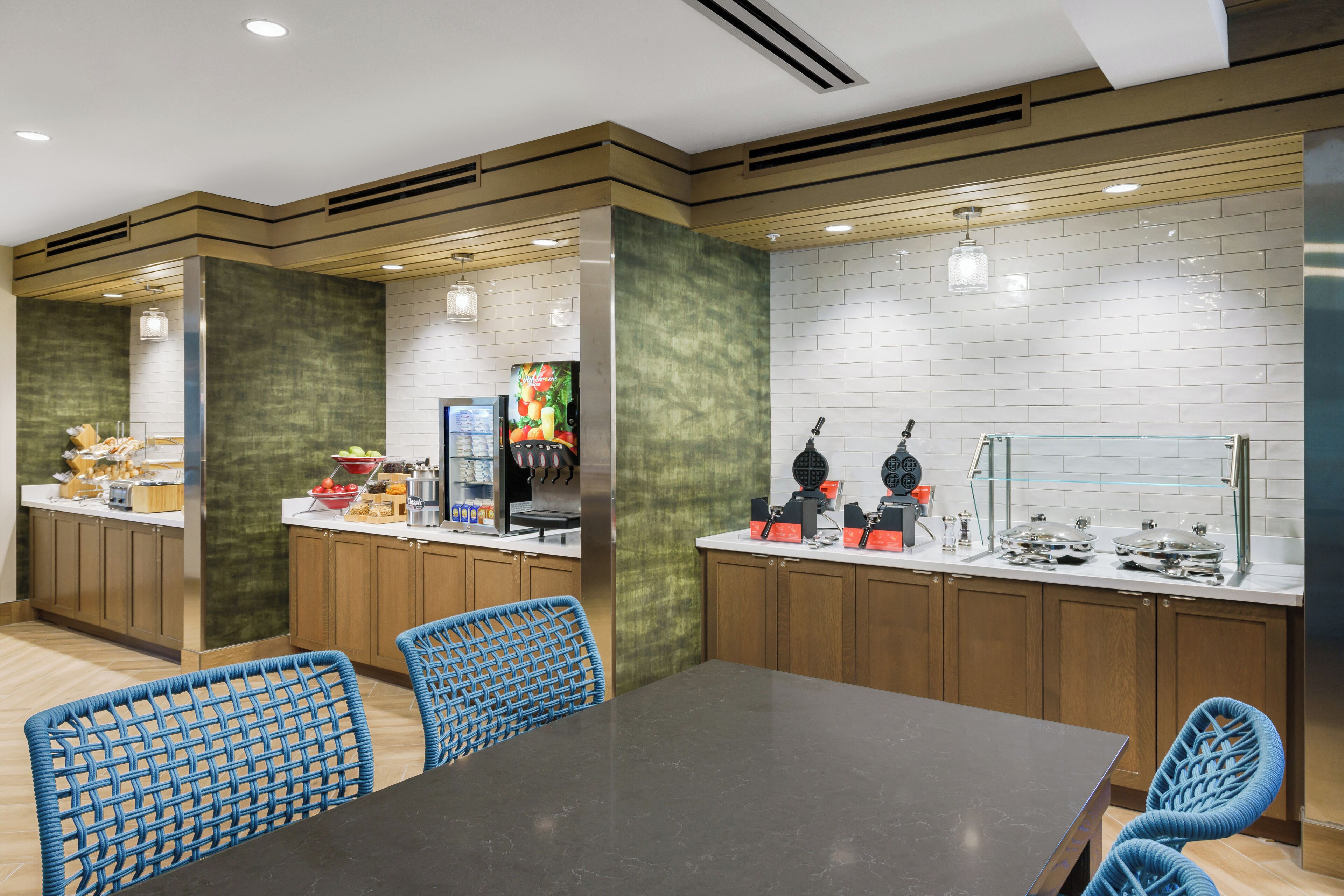 A modern kitchen with wooden cabinets, a black countertop, and blue woven chairs.