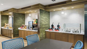 A modern kitchen with wooden cabinets, a black countertop, and blue woven chairs.