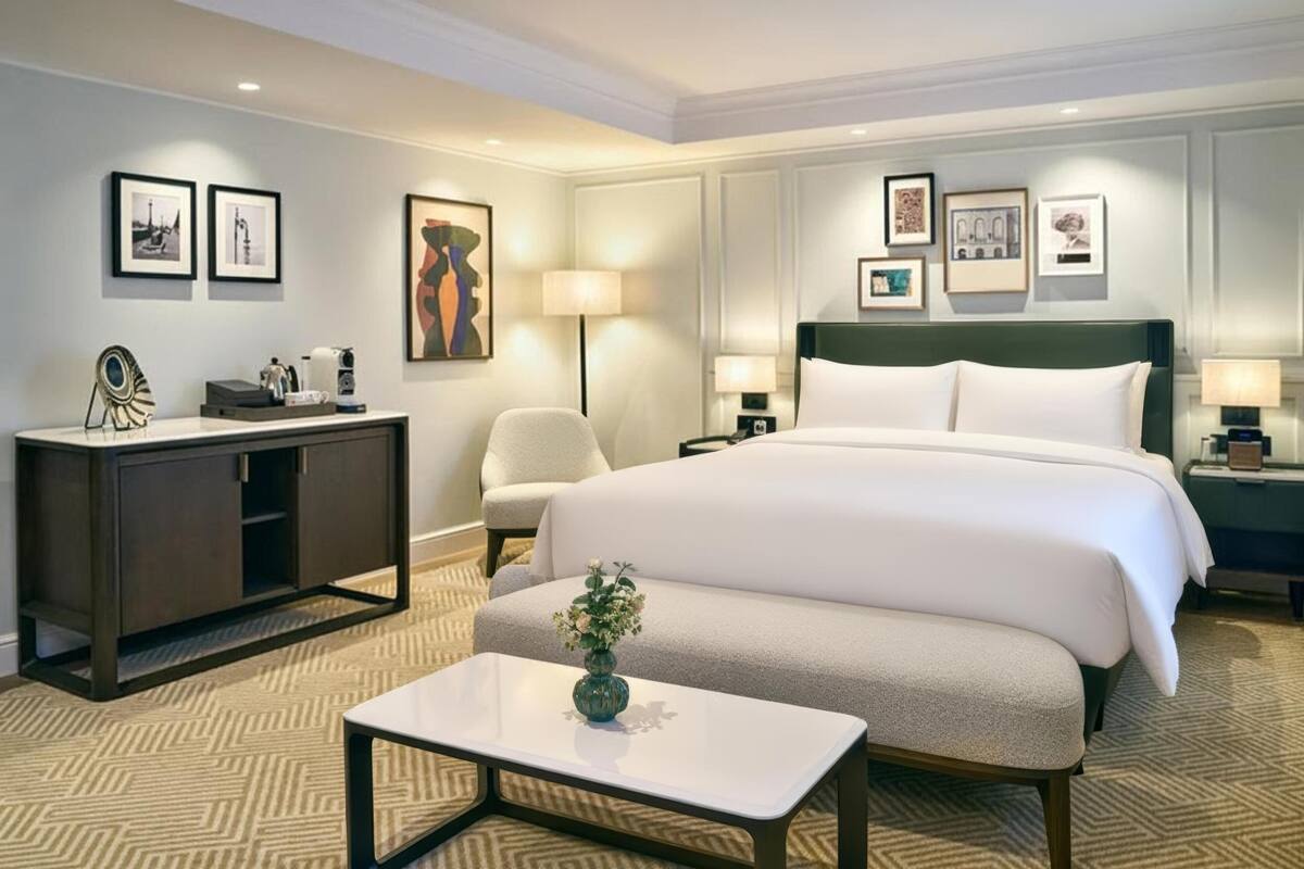 Une chambre d’hôtel avec un grand lit, un bureau, une chaise et une petite table sur laquelle se trouve un vase.