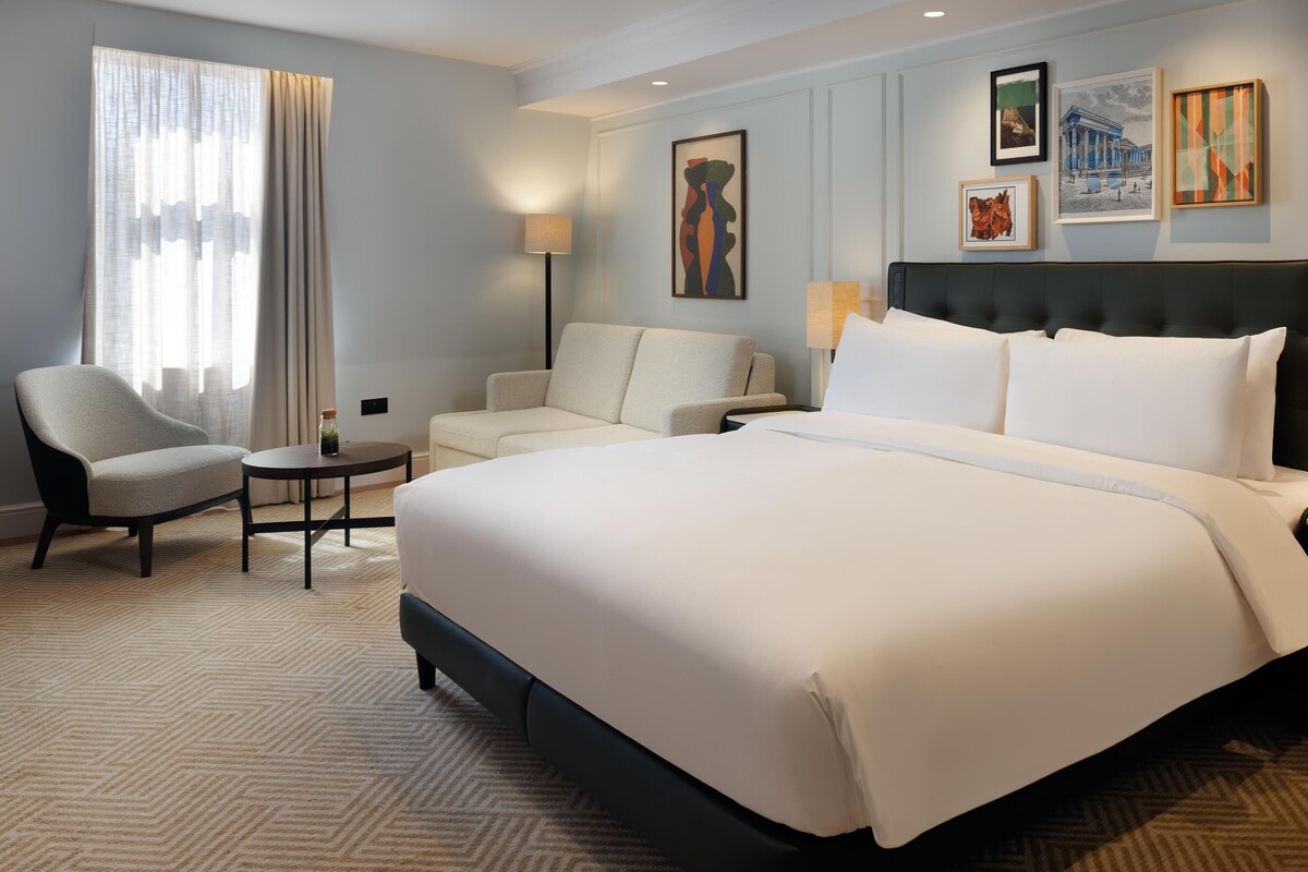 A hotel room with a large bed, two armchairs, a small table, and artwork on the walls.