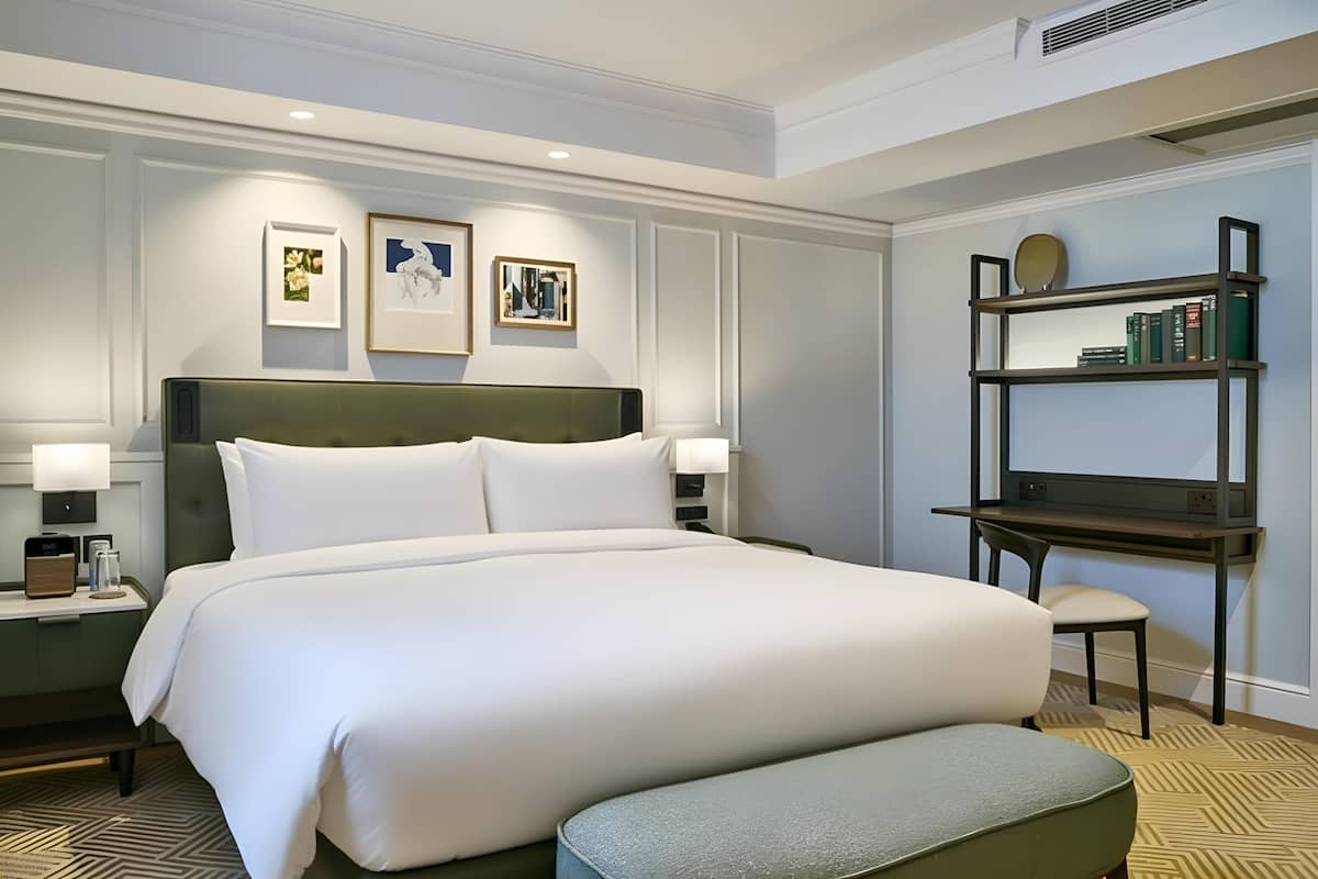 Une chambre d’hôtel avec un grand lit, des tables de chevet, une bibliothèque et des œuvres d’art encadrées accrochées au mur.