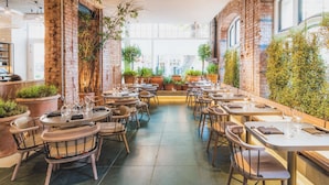 A restaurant with brick walls, potted plants, and round tables with chairs. - Radisson Blu Hotel, London Bloomsbury (London)