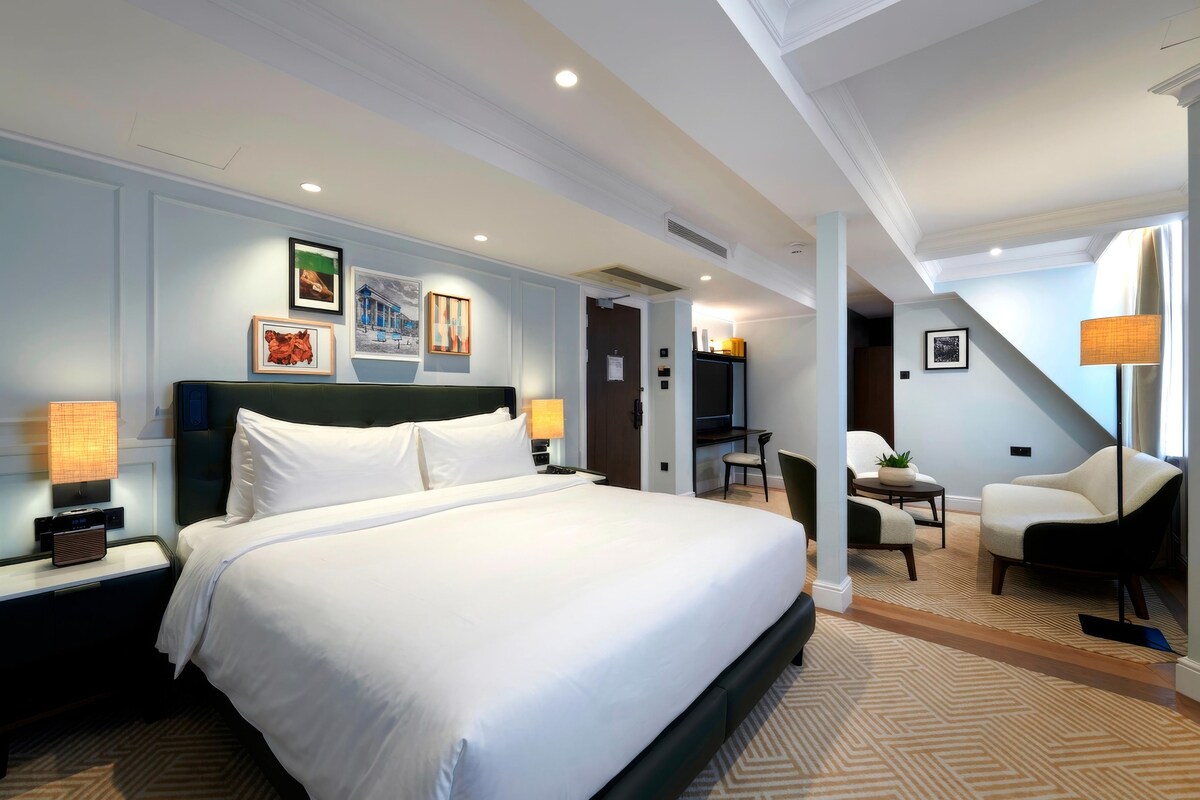 A hotel room with a large bed, a desk, a chair, and a TV.