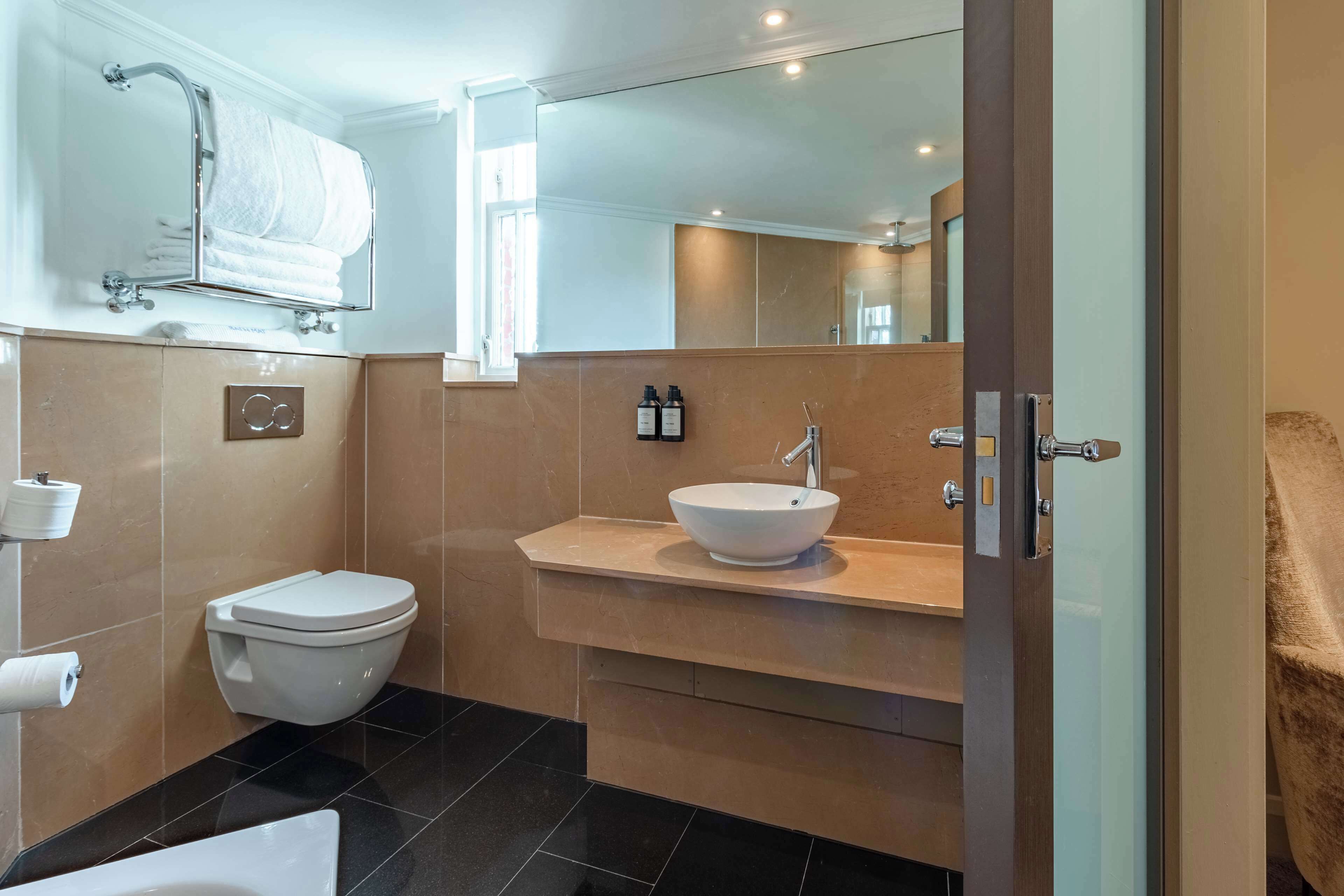 A modern bathroom with a white toilet, a large mirror, a white sink, and a towel rack.