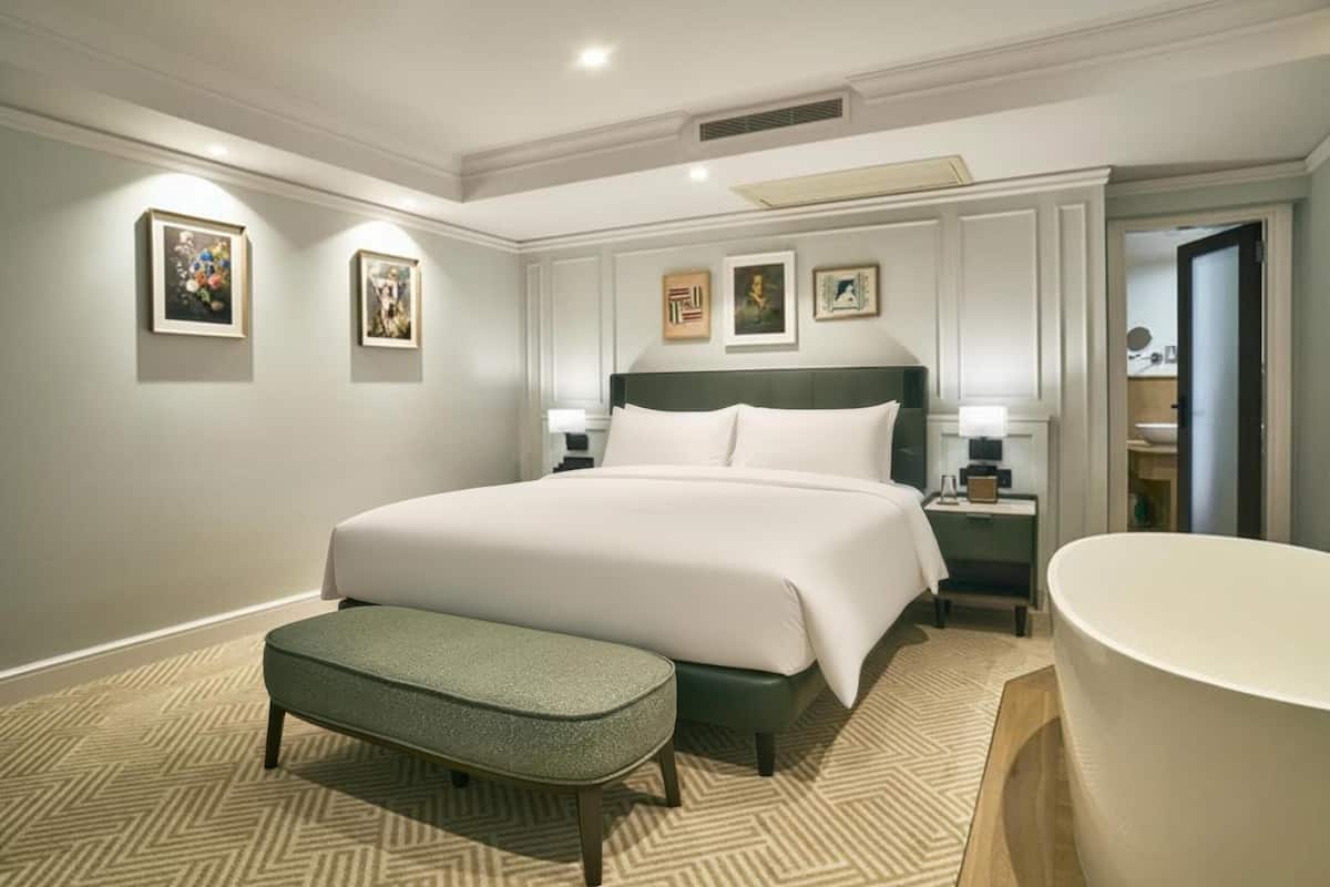 Une chambre d’hôtel moderne dotée d’un grand lit, d’un coin salon, d’une baignoire et d’œuvres d’art encadrées accrochées aux murs.