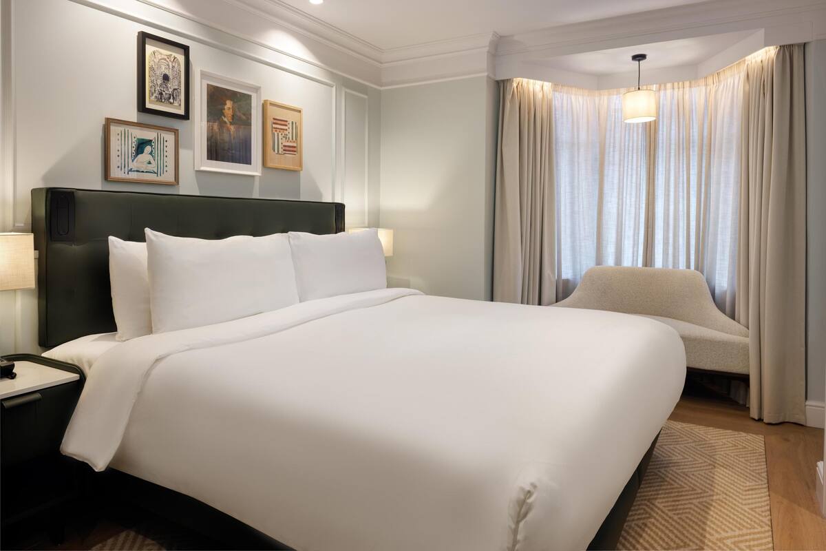 Une chambre d’hôtel avec un grand lit, une chaise, une table de chevet et un mur orné de tableaux.