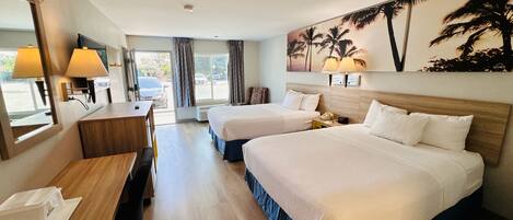 A hotel room with two beds, a desk, a chair, a TV, and a painting of palm trees.
