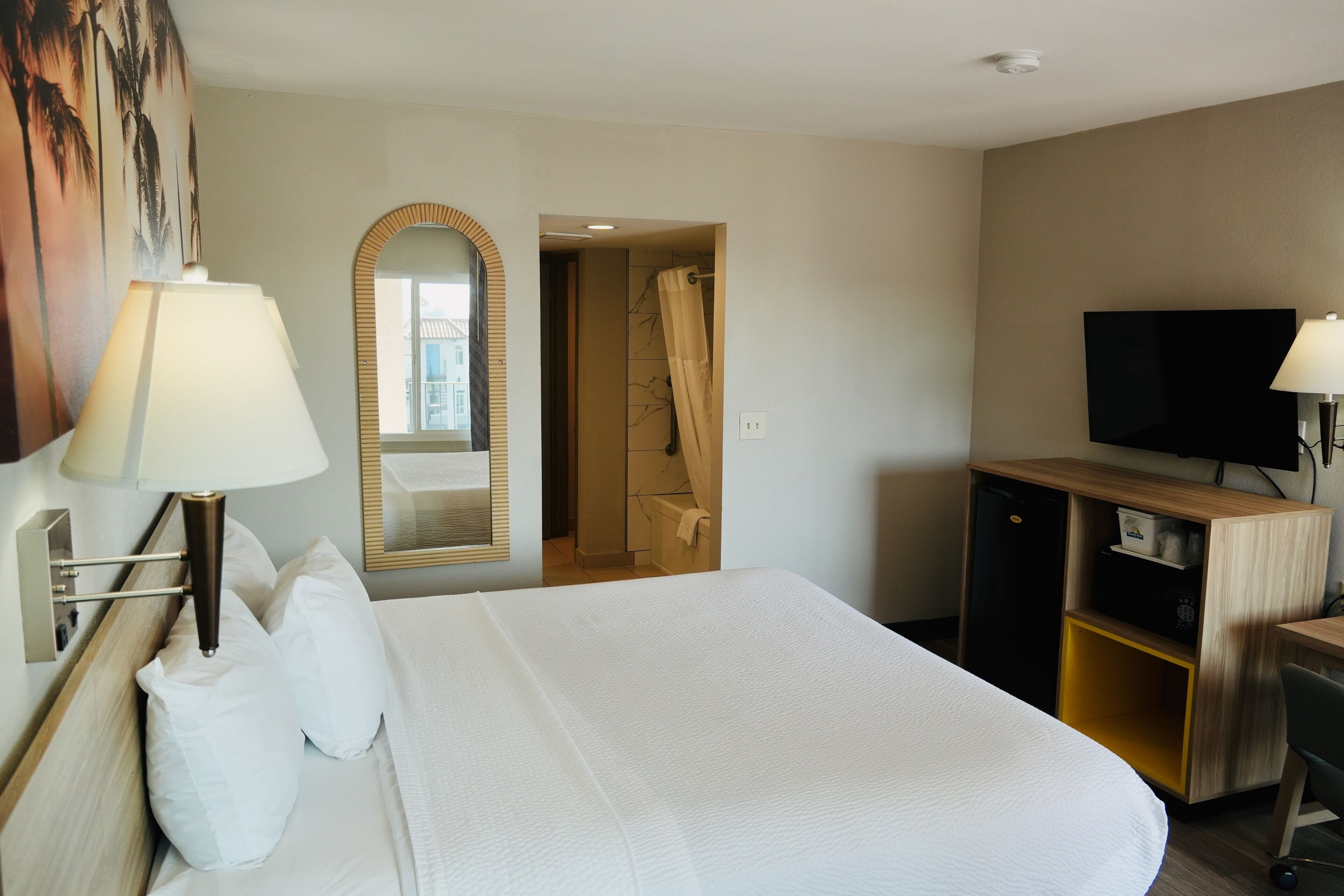 Habitación de hotel con una cama grande, televisión, escritorio y baño visible a través de una puerta abierta.