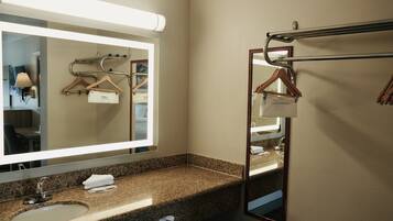 A hotel bathroom with a granite countertop sink, a large mirror, towel racks, and a towel dispenser.