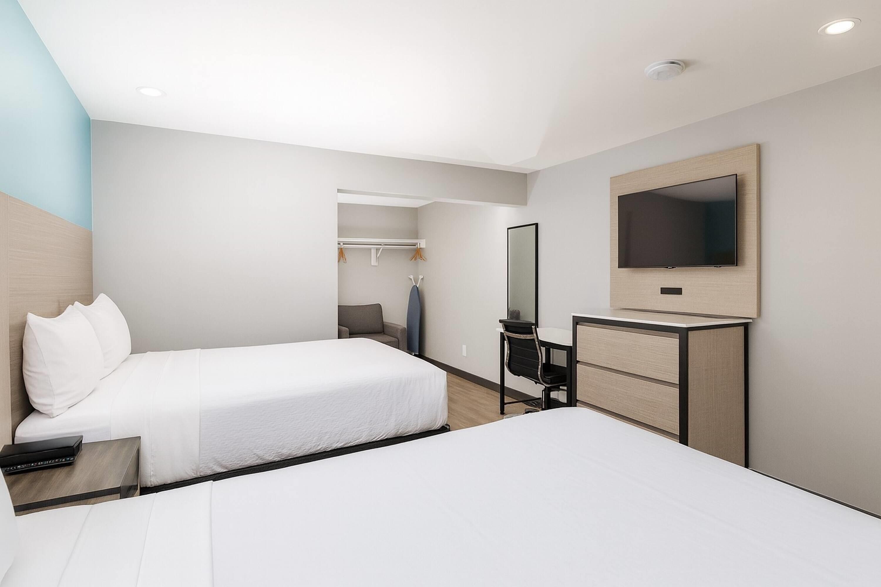 Habitación de hotel con dos camas, un escritorio, una silla, un televisor y un armario.