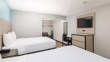 Habitación de hotel con dos camas, un escritorio, una silla, un televisor y un armario.