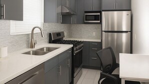 Una cocina moderna con gabinetes grises, electrodomésticos de acero inoxidable, una encimera blanca y una silla de oficina negra.