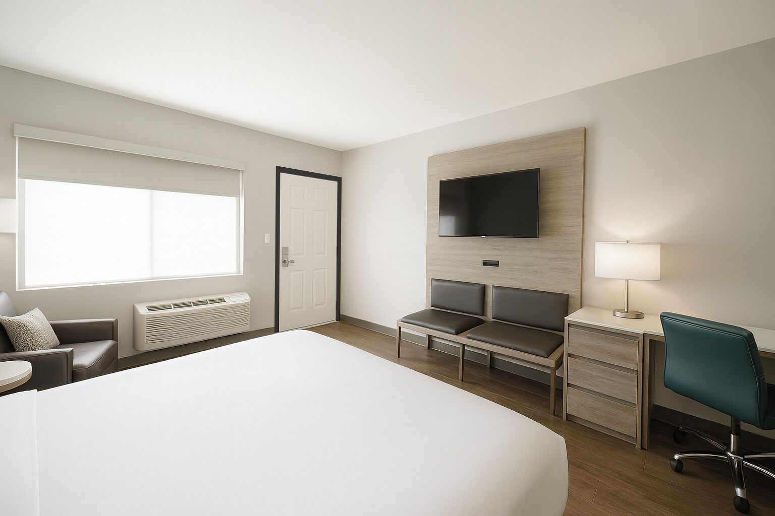 A hotel room with a large bed, a desk with a chair, a TV mounted on the wall, and a window with blinds.