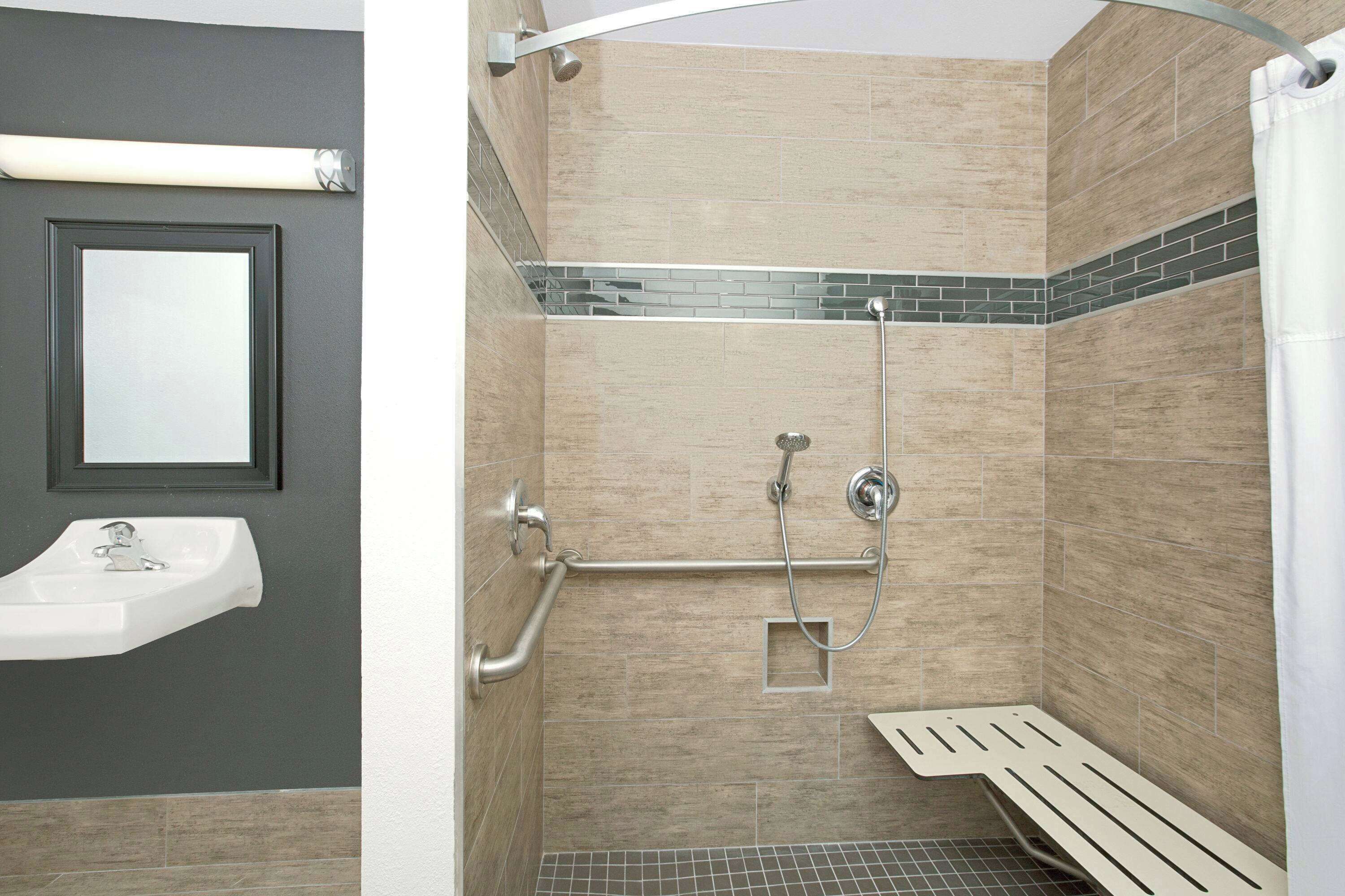 A shower with a grab bar, a wall-mounted sink, and a tiled shower area.
