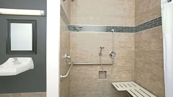 Una ducha con barra de apoyo, lavamanos fijado a la pared y zona de ducha con azulejos.