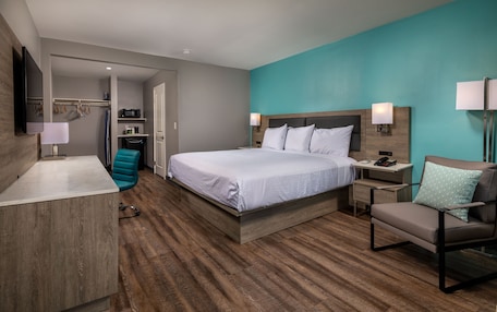 A modern hotel room with a large bed, a desk, a chair, and a TV.