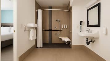 A hotel bathroom with a shower, a sink, a mirror, and a towel rack.