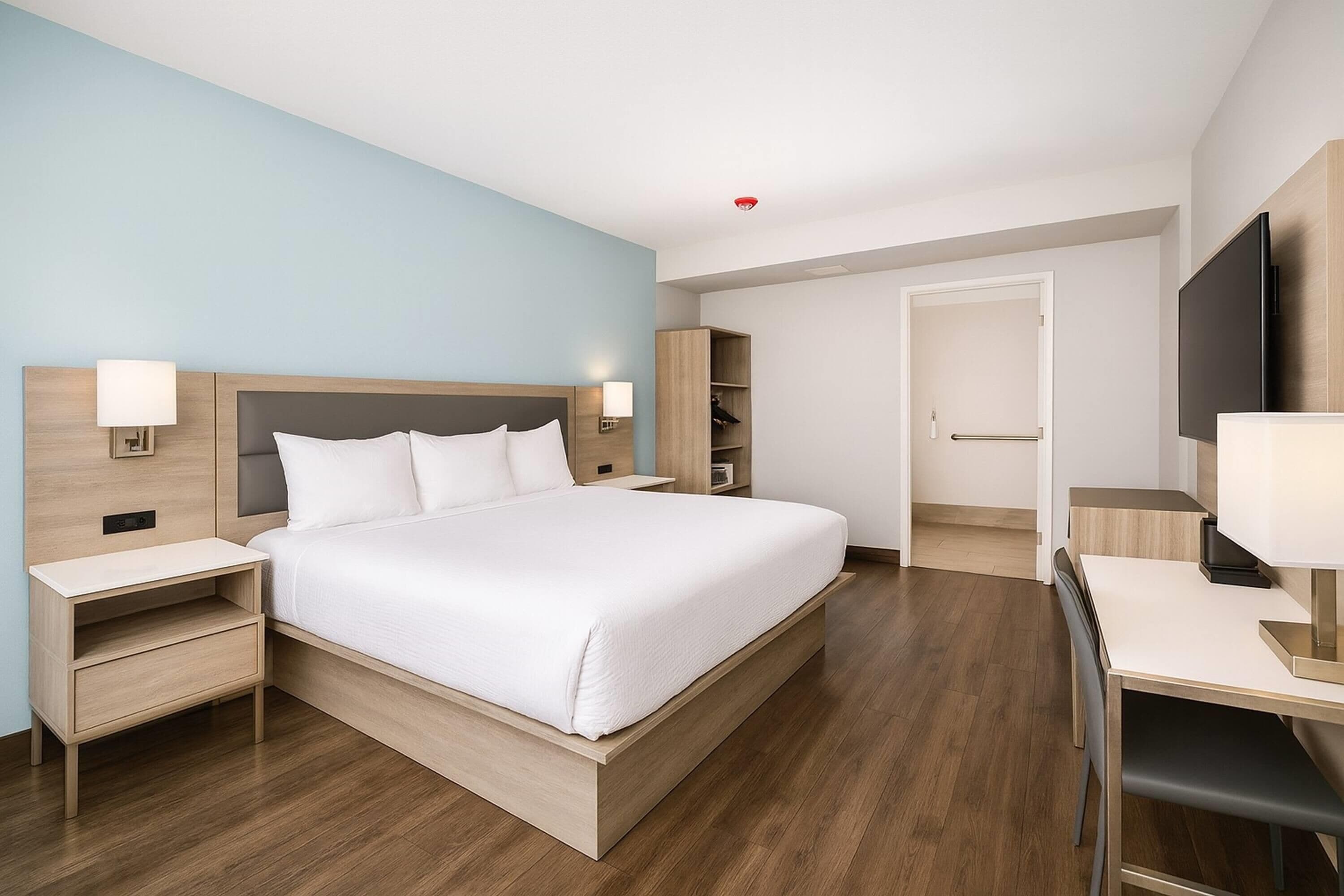 A modern hotel room with a large bed, bedside tables, a desk, and a TV.
